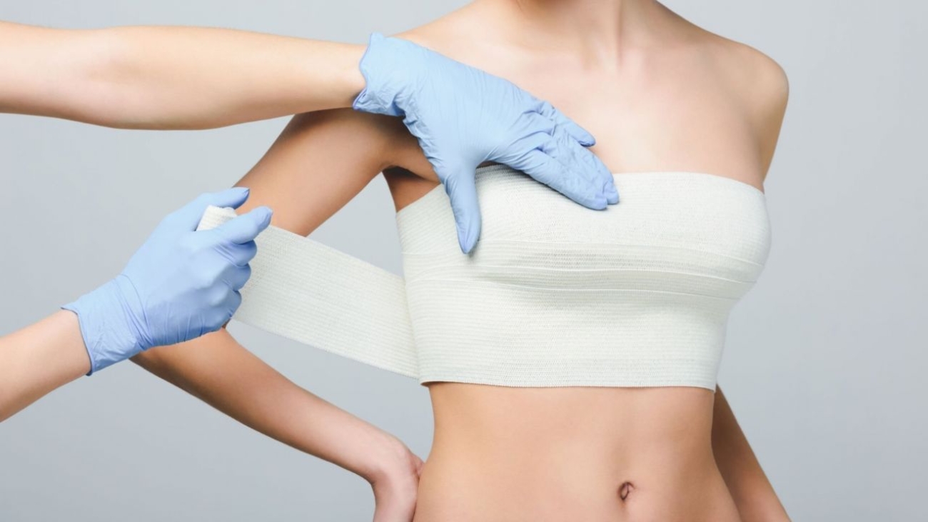Cirurgião plástico envolve paciente com faixa após cirurgia de mastopexia